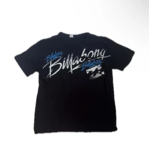 Svart Billabong t-shirt med tryck - Svart t-shirt från Billabong med stort grafiskt tryck i vitt och blått framtill. Klassisk passform med rund hals och korta ärmar. Perfekt för dig som gillar streetwear och surf vibes. Materialet känns mjukt och skönt mot huden.