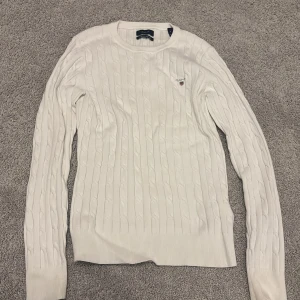 Vit kabelstickad tröja från Gant - Vit kabelstickad tröja från Gant med rund halsringning och broderad logga på bröstet. Tröjan har långa ärmar och ribbade muddar vid ärmslut och nederkant. Nyskick, använd mycket fåtal gånger. Nypris 1600kr, säljer nu för 200kr