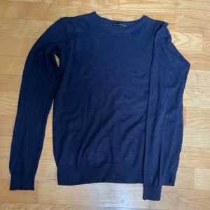 Mörkblå stickad tröja Daniele Alessandrini - Mörkblå stickad tröja från Daniele Alessandrini med rund halsringning och lång ärm. Tröjan har en diskret broderad detalj vid axeln och ribbade muddar vid ärmslut och nederkant. 