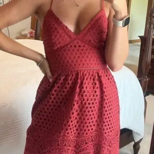 Röd spetsklänning med smala axelband - Superfin röd klänning med smala justerbara axelband och v-ringning. Klänningen har ett snyggt hålmönster i spets och är fodrad. Midjan är markerad och nederkanten har fina spetsdetaljer. 