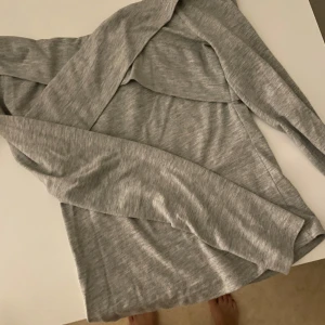 Grå omlottop från Bik Bok - Säljer en ljusgrå omlottop från Bik Bok i mjuk bomullsblandning. Toppen har lång ärm och en snygg omlottdesign framtill som ger en trendig look. Perfekt att styla med jeans eller kjol för en chill vibe.