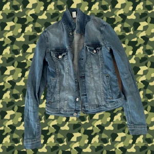 Klassisk blå jeansjacka - Snygg blå jeansjacka med knappar framtill och två bröstfickor med lock. Jackan har en klassisk passform och långa ärmar, perfekt att slänga över en hoodie eller t-shirt. Tidlös denimstil som alltid funkar.