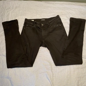 Svarta slim jeans Jack & Jones - Svarta slim fit jeans från Jack & Jones, modell Glenn. Klassisk femficksdesign, smal passform och diskreta svarta sömmar. Jeansen är tillverkade i stretchig bomullsblandning för extra komfort och har en stilren look som funkar till det mesta.