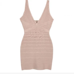 Beige tight kort klänning med v-ringning - Supersnygg beige kort klänning med djup v-ringning och breda axelband. Klänningen har en figurnära passform och ribbade detaljer som ger en cool struktur. Perfekt för dig som vill sticka ut med en stilren och modern look. Bandage klänning