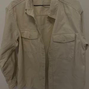 Beige manchester overshirt - Stilren beige overshirt i mjuk manchester med klassisk krage och två stora bröstfickor med knappar. Perfekt att slänga över en t-shirt för en avslappnad look. Långärmad och med knäppning framtill.