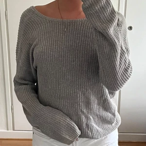 Grå stickad tröja med öppen rygg - Säljer en grå stickad tröja med bred, rund halsringning och snygg öppen rygg. Tröjan har lång ärm och en loose fit som ger en chill vibe. Perfekt att slänga på sig över ett linne eller bara som den är. Superenkel att matcha till allt!