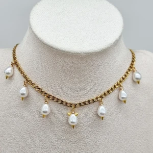 Guldfärgat halsband med pärldroppar - Stilrent halsband med kraftig guldfärgad kedja och sju hängande droppformade pärlor. Pärlorna är vita och har små guldfärgade detaljer i toppen och botten. Perfekt statement-piece för att lyfta din look.