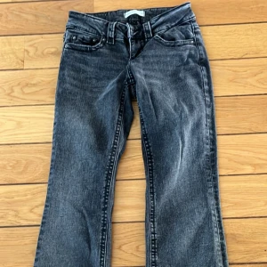 Svarta bootcut jeans med knappar - Snygga svarta jeans med bootcut passform och slitna detaljer. Byxorna har klassiska fem fickor, coola knappar på bakfickorna och en lätt tvättad look. Perfekta för dig som gillar en avslappnad men trendig stil.