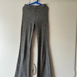 Grå ribbade bootcut-byxor H&M Divided - Grå ribbade byxor från H&M Divided i bootcut-modell. Byxorna har hög midja och är tillverkade i mjukt, stretchigt material som sitter skönt. Perfekta för en chill och trendig look med sin vida passform nertill.