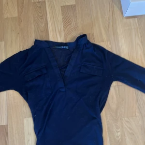 Mörkblå blus från Atmosphere - Snygg mörkblå blus från Atmosphere med v-ringning och två fickor. Ärmarna kan rullas upp och fästas med knapp. Tunn och lätt i materialet, perfekt för vår och sommar. 