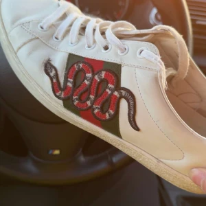 Gucci Ace sneakers med orm brodyr - Gucci Ace sneakers i vitt skinn med ikoniska gröna och röda ränder på sidan och broderad orm. Klassisk låg modell med snörning och GG-mönstrad innersula. Perfekta för dig som vill sticka ut med lyxig streetstyle. Box o påsar tillkommer med köp pris kan diskuteras