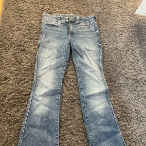 Blå bootcut jeans från H&M, stl 164 - Snygga blå bootcut jeans från H&M i storlek 164. Jeansen har låg midja, justerbar midja och klassisk femficksdesign med coola detaljer på bakfickorna. Materialet är jeans med lätt slitning för en avslappnad look.