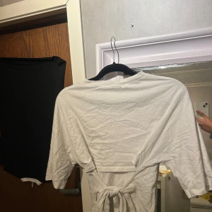 Vit t-shirt med knyt från Nelly - Säljer en vit t-shirt från Nelly. T-shirten har korta ärmar, rund halsringning och snygg knytning i ryggen som ger en unik look. Perfekt till jeans eller kjol för en chill vibe. Köpt för 300 (Tänk på att den inte är strykt)  