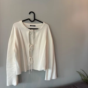 Vit stickad kofta med snörning Gina Tricot - Vit stickad kofta från Gina Tricot med croppad passform och långa ärmar. Framsidan har trendig snörning med tre knyt längs öppningen. Perfekt för lager-på-lager och ger en chill men snygg vibe.