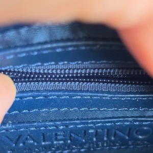 Mörkblå sammet axelväska Valentino - Supersnygg mörkblå axelväska från Valentino i lyxig sammet med guldfärgad kedja och V-detalj framtill. Väskan har dekorativa fransar i metall och dragkedja inuti. Perfekt storlek för det viktigaste och ger en riktigt elegant vibe.