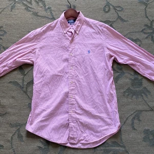 Rosa randig skjorta från Polo Ralph Lauren - Säljer en rosa och vit randig skjorta från Polo Ralph Lauren i custom fit. Mycket bra skick, behöver bara strykas😉 nypris 1900