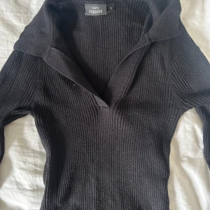 Svart ribbad tröja från KappAhl - Svart ribbad långärmad tröja från KappAhl med v-ringad krage. Sitter tight och har en klassisk, stilren look som funkar till allt. Mjuk och stretchig i materialet, perfekt för lager på lager under höst och vinter.