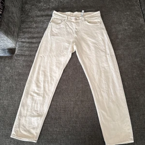 Beige Barrel jeans från Weekday W28 L30 - Säljer ett par beige Barrel Relaxed Tapered jeans från Weekday i storlek W28 L30. Jeansen har en avslappnad passform med avsmalnande ben, klassisk femficksdesign och bälteshällor. Perfekta för dig som gillar en clean och stilren look.