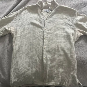 Beige skjorta från SMOG i bomull - Luftig och avslappnad beige skjorta från SMOG i storlek L. Skjortan har ett diskret rutigt mönster i strukturen, knappar framtill och en relaxed fit. Perfekt för dig som gillar en chill och stilren vibe.