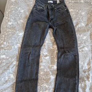 Grå raka jeans från Zara - Snygga grå jeans från Zara i rak modell med råa kanter nertill. Klassisk femficksdesign och normal passform. Jeansen är tillverkade i bomull och har en mörkgrå tvätt som ger en cool vintagekänsla.