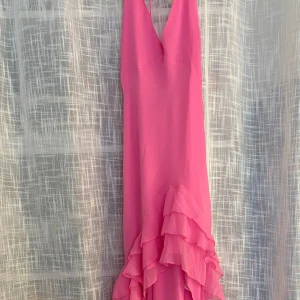 Lång rosa klänning med volanger - Säljer en superfin lång klänning i stark rosa med v-ringad hals och tunna axelband. Klänningen har flera lager volanger längs nederdelen som ger en riktigt flowy och cool look. Perfekt för dig som vill sticka ut och älskar färg! Materialet känns lätt och luftigt.