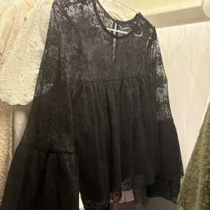 Svart spetsblus med vida ärmar - Supersnygg svart blus från Gina Tricot i transparent spets med voluminösa, vida ärmar och rund halsringning. Blusen har en flowy passform och fina spetsdetaljer som ger en cool och romantisk vibe. Perfekt att styla med jeans eller kjol för en trendig look. Säljer för att den inte används, Nästan aldrig användt fast ett litet hål på armen men inget man tänker på.