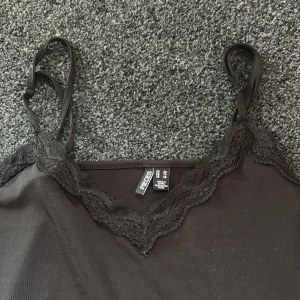 Svart spetslinnetopp från Pieces - Svart linne från Pieces med smala axelband och v-ringad halsringning dekorerad med spets finns inga tecken på användning och i toppen skick skriv om ni har funderingar🤗
