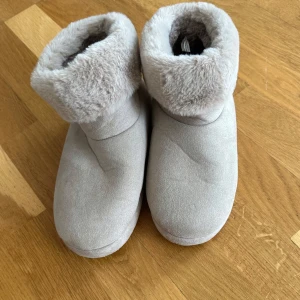Beiga fluffiga boots med fuskpäls - Mysiga boots i ljusbeige med mjuk fuskpäls runt skaftet och insidan. Ovandel i mockaliknande material och platt sula med små prickar undertill för extra grepp. Perfekta för kalla dagar när du vill hålla fötterna varma.