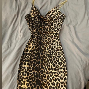 Leopardmönstrad kort klänning LoverY - Säljer en snygg leopardmönstrad kort klänning från LoverY med guldfärgade kedjeaxelband. Klänningen har figurnära passform och cool drapering vid bysten. Perfekt för dig som vill sticka ut med ett djuriskt mönster och guldiga detaljer.