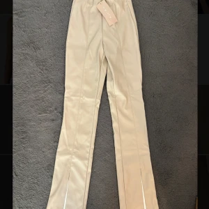 Beiga byxor i skinnimitation från new Yorker  - Snygga beiga byxor från new Yorker i skinnimitation med hög midja och raka ben. Byxorna har diskreta sömmar framtill och slits vid benslutet. Aldrig använda och prislappen på. Skriv för fler bilder🥰