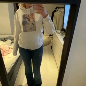 Vit hoodie med konsttryck från The Cool Elephant - Säljer en vit hoodie från The Cool Elephant i storlek S. Tröjan har ett färgstarkt konsttryck med ansikte och abstrakta detaljer på bröstet, snörning vid huvan och en klassisk magficka. Perfekt för dig som gillar unika och kreativa plagg.