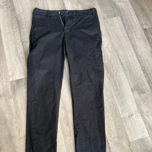Svarta chinos med raka ben - Snygga svarta chinos med raka ben och klassisk passform. Byxorna har bälteshällor, sidfickor fram och knäppning med dragkedja. Bakfickor med knapp för en clean look. Perfekta till en stilren outfit.