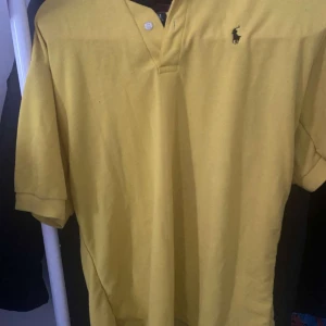 Gul pikétröja från Polo Ralph Lauren XL - Gul pikétröja från Polo Ralph Lauren i 100% bomull. Klassisk piké med korta ärmar, krage och två knappar vid halsen. Ikoniska broderade loggan i svart på bröstet. Perfekt för dig som gillar en clean och sportig stil.