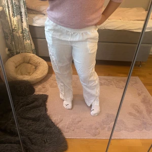 Vita linnebyxor med resårmidja - Säljer ett par vita linnebyxor med avslappnad passform och resår i midjan. Byxorna har dragsko och sidfickor, perfekta för en chill och luftig stil. Materialet är svalt linne och färgen är helvit, vilket gör dem enkla att matcha med allt.