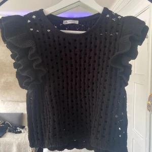 Svart stickad topp med volangärm Zara - Svart stickad topp från Zara med grov hålstickning och stora volangärmar. Den är kort så den upplevs som XS i storleken. Knappt använd och för liten, helt i nytt skick.
