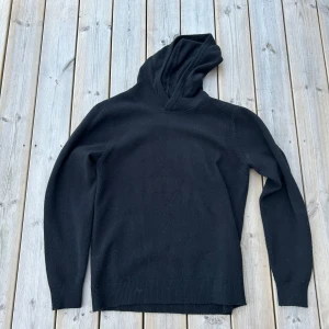 Merinoull hoodie - Svart hoodie från Vailent i mjuk merinoull. Tröjan har lång ärm, ribbade muddar och en klassisk huva. Perfekt för dig som gillar stilrena och bekväma plagg med enkel design. Passar dig som vill ha en varm och skön tröja under kyliga dagar.
