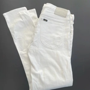 Vita jeans från Lee - Säljer ett par klassiska vita jeans från Lee med fem fickor och silverfärgade nitar. Byxorna har normal passform och raka ben. Perfekta för en stilren look och lätta att matcha med olika outfits.