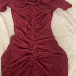 Vinröd kortklänning med snörning - Säljer en vinröd kortklänning med snygg snörning längs hela framsidan. Klänningen har korta ärmar och en figurnära passform som framhäver siluetten. Perfekt för dig som gillar trendiga detaljer och en cool look.