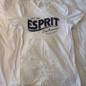 Vit t-shirt från Esprit med tryck - Vit t-shirt från Esprit med stort blått tryck på bröstet där det står 'ESPRIT San Francisco'. Klassisk rund hals och korta ärmar. Perfekt för dig som gillar enkel och stilren streetwear med en touch av retro.