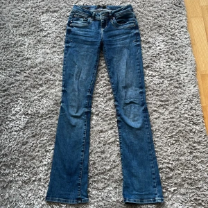LTB Valerie bootcut jeans blå - Snygga blå jeans från LTB, modell Valerie, med klassisk bootcut och femficksdesign. Jeansen har ljus tvätt, kontrastsömmar och en stilren broderad bakficka. Perfekta för dig som gillar en tidlös och avslappnad look.