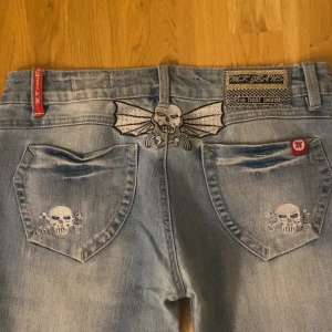 Ljusblå MK Jeans med döskallebrodyr - Säljer ett par ljusblå jeans från MK Jeans med grymma döskallebroderier på bakfickorna💕 De var tyvärr för stora på mig därav säljer jag de🫶🏻Midjevidd 39 cm, benvidd 24 cm, längd 106 cm. Pris går att diskutera ‼️