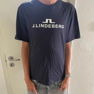 Mörkblå J.Lindeberg t-shirt med logga - Tjenare säljer denna unika mörkblå t-shirt från J.Lindeberg med vit logotyp tryckt på bröstet. T-shirten är använd fåtals gånger 10/10 skick. Ny pris: 699kr.  Mitt pris: 325kr. Tveka inte att höra av er! Mvh ville 
