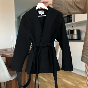 Svart omlottkappa från NA-KD - Stilren svart omlottkappa från NA-KD med bälte i midjan och stora fickor framtill. (Moa Mattson kollektion) köpte för 1000 kr andvönd en gång st är 36