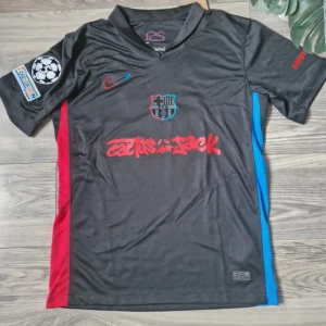 FC Barcelona Lamine Yamal tröja svart - Snygg svart FC Barcelona fotbollströja från Nike med Lamine Yamal och nummer 19 på ryggen. Tröjan har röda och blå detaljer på sidorna, klubbmärke på bröstet och Champions League-märke på ärmen. Tillverkad i lätt och ventilerande material, perfekt för match eller träning.