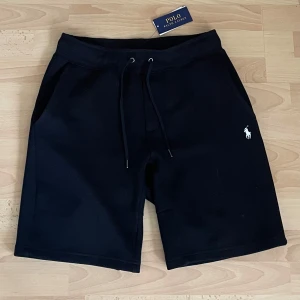 Ralph Lauren shorts - Storlek M . Nytt skick .Svarta shorts från Polo Ralph Lauren med klassisk vit broderad logga på benet. Modellen har snörning i midjan och är tillverkad i mjuk bomull, perfekt för chill dagar. Snygg och enkel design med fickor på sidorna och relaxed fit.