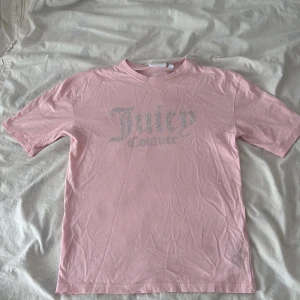 Rosa Juicy Couture t-shirt med strass - Snygg ljusrosa t-shirt från Juicy Couture med glittrande strasslogga på bröstet. Klassisk rund hals och korta ärmar. Mjuk och skön bomull som känns chill mot huden. Perfekt för dig som gillar en feminin vibe och vill sticka ut med lite bling. Nytt pris 399 men har en liten fläck vid märket men den går bort i tvätten är jag säker på!