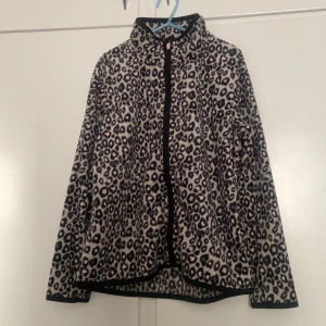Leopardmönstrad fleecejacka  - Säljer en leopardmönstrad fleecejacka svart, grått och vitt. Jackan har hel dragkedja framtill, hög krage och svarta kantband. Perfekt för dig vill ha något mjukt och skönt. 