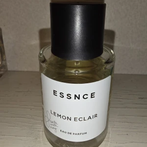 ESSNCE Lemon Eclair Eau de Parfum - Fräsch parfym med citrusdoft från ESSNCE, Lemon Eclair. Kommer i en rund, transparent glasflaska med svart cylinderformat lock och vit etikett. Perfekt för dig som gillar lätta och fruktiga dofter med en modern touch.