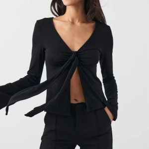 Svart långärmad knyttopp Gina Tricot - Trendig svart långärmad topp från Gina Tricot med djup v-ringning och knyt framtill. Modellen är croppad och har en snygg, figurnära passform. Perfekt att styla med höga byxor för en cool look. Bara använt några få ggr☺️