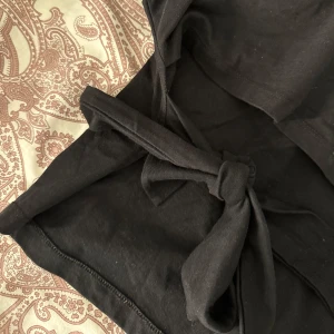 Svart kort klänning från Nelly - Säljer en svart topp från Nelly i storlek S. Toppen har en snygg knyt-detalj bak som ger en cool och trendig look. Materialet är mjukt och känns bekvämt mot huden, perfekt för dig som gillar stilrena och enkla plagg. (Ser smutsig ut men det är bara damm, tvättas givetvis innan ja postar)